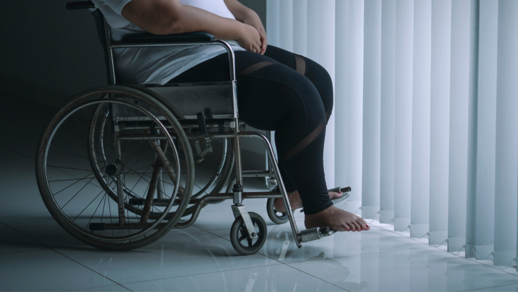 Photo of a woman sitting in a wheelchair. Her face and upper body are not visible. She is barefoot and wearing athletic leggings.