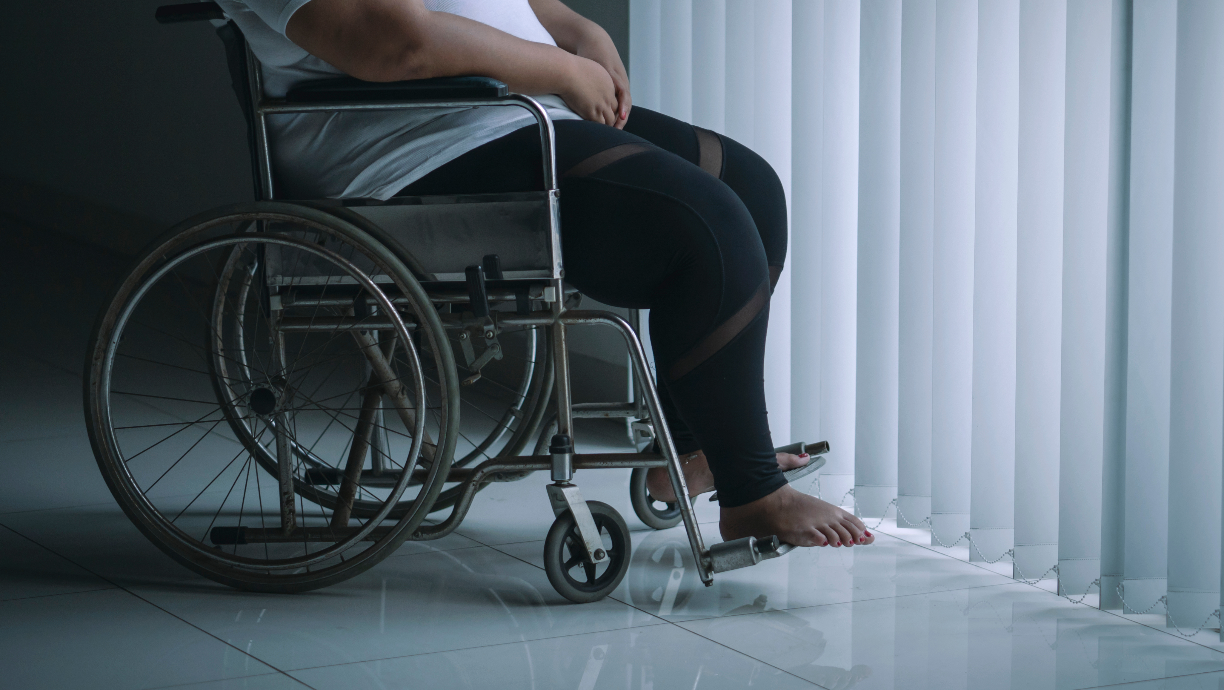 Photo of a woman sitting in a wheelchair. Her face and upper body are not visible. She is barefoot and wearing athletic leggings.